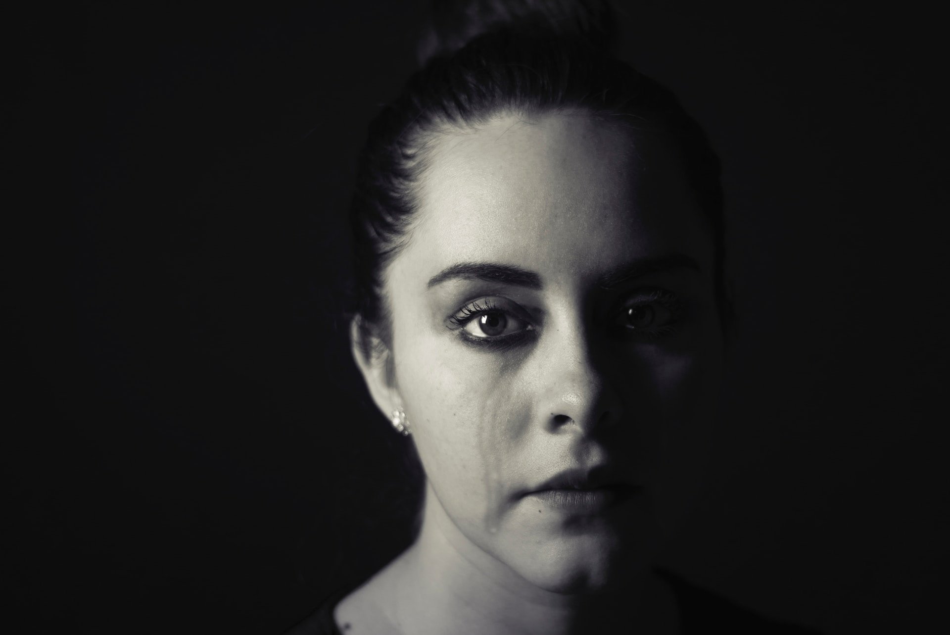 Imaginea unei femei plângând în întuneric simbolizează durerea tăcută a abuzului domestic; articolul nostru explorează călătoria de la suferință la renaștere și oferă strategii de vindecare și suport pentru supraviețuitori